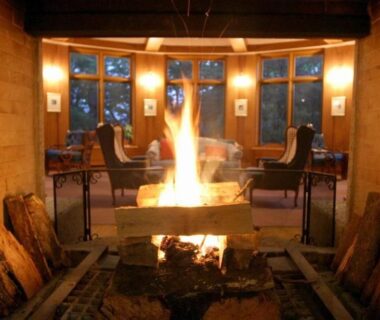 Central wood-burning fireplace with armchairs and tall windows in Chuzenji Kanaya Hotel lounge, Tochigi