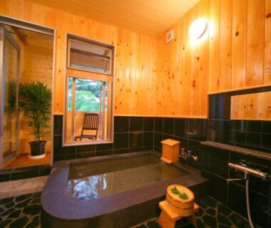 Wooden bathing room with stone tub and stools at Chuzenji Pension in Tochigi, Japan