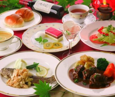 Multi-course Western meal with salad, bread, wine and desserts on red tablecloth in ryokan dining room