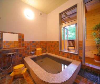 Tiled indoor onsen tub with wooden stools, shower fixtures and window view at Chuzenji Pension, Tochigi