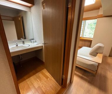Sink and bathroom doorway leading to wood-floored guest room with seating at Club Wyndham Shirakabaso Shigakogen, Nagano