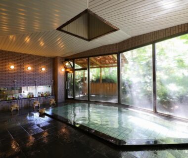 Indoor onsen with stone-edged bath and large windows at Club Wyndham Shirakabaso Shigakogen Nagano