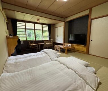 Japanese tatami room with two futons, low table, shoji screens and greenery visible through window at a Nagano ryokan