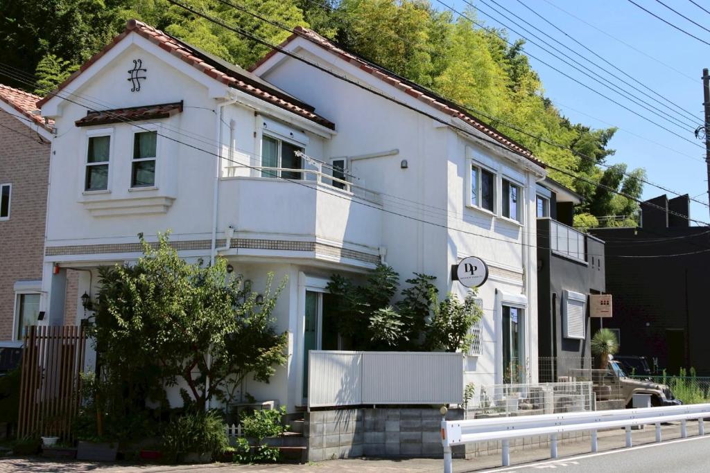 White guesthouse exterior DP小山町Machida Tokyo Kantō Two-story white guesthouse facade with balcony, small front greenery and bamboo backdrop, DP小山町Machida, Tokyo