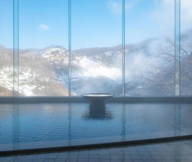 Indoor onsen bath with floor-to-ceiling windows framing snow-covered mountains at Dai-ichi Takimotokan Hokkaidō