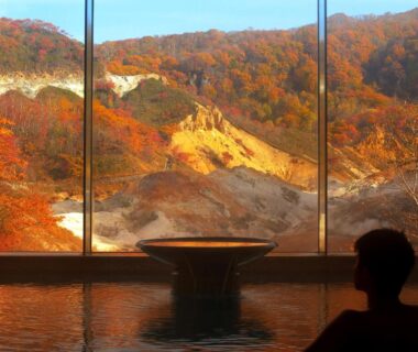 Indoor onsen bath facing autumn mountains through floor-to-ceiling window at Dai-ichi Takimotokan, Hokkaidō