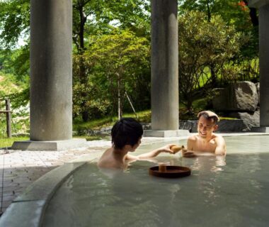 Two guests relaxing in a stone onsen bath with columns and garden at Dai-ichi Takimotokan, Hokkaidō