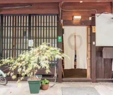 Noren curtain at a traditional wooden entrance with potted plants and a bicycle, Daitokuji Sushicho, Kyoto