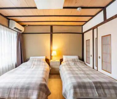 Twin beds on tatami floor with shoji screens, bedside lamp and wooden ceiling beams at Daitokuji Sushicho Kyoto