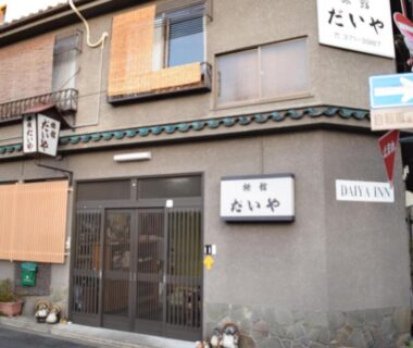Traditional two-story ryokan facade with sliding entrance and signage on a narrow Kyoto street