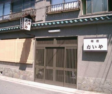 Exterior of Daiya Ryokan showing wooden sliding doors, signboard, bamboo blind and stone foundation on a narrow Kyoto street