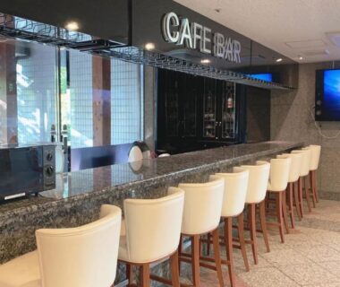 Upholstered bar stools along marble counter at hotel cafe bar with wall television at Day Nice Hotel Tokyo