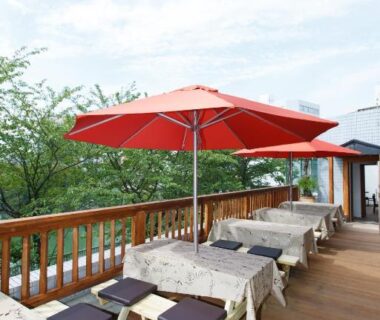 Outdoor wooden terrace with red umbrellas and bench seating at Day Nice Hotel Tokyo, Tokyo, Kantō, Japan