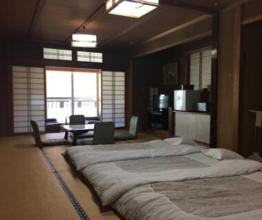 Spacious tatami room with futons, low table and shoji screens at Daymaruya Ryokan in Nagano