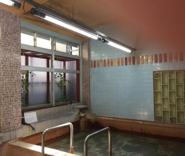 Tiled indoor onsen bath with metal handrails, frosted window and mosaic tiles at Daymaruya Ryokan, Nagano