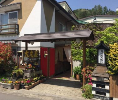Entrance with noren, potted flowers, wooden lantern and signage at Daymaruya Ryokan in Nagano