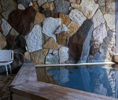 Indoor onsen bath with stone feature wall and wooden edge at Donkairo, Hyōgo