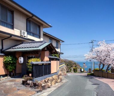 Ryokan entrance framed by cherry blossoms and seaside view at Donkairo, Hyōgo, Kansai