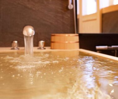 Indoor wooden soaking tub with flowing faucet and wooden bucket at Takeda Castle Town Hotel, Hyōgo