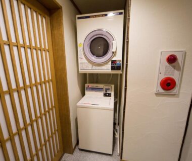 Compact laundry corner with stacked washer and dryer beside shoji screen at Ebisu Ryokan in Kyoto