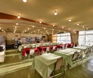 Spacious communal dining room with neatly arranged tables and chairs, large windows and overhead lighting at Eboshiso in Iwate