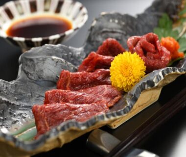 Thin raw sliced meat with yellow chrysanthemum garnish and soy dipping sauce on decorative platter at Eirakukan, Fukushima