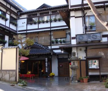 Multi-story traditional ryokan facade with entrance lantern, shoji windows and courtyard seating at Ekinariya Ryokan, Gunma