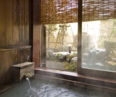 Wooden indoor onsen bath with flowing water and small garden view at Ekinariya Ryokan, Gunma