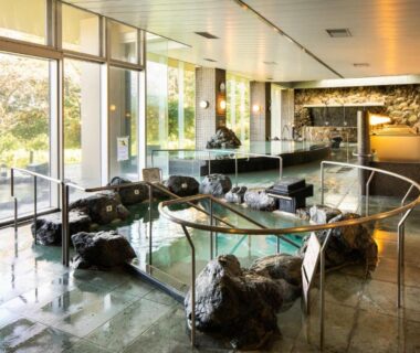 Indoor onsen bath with natural rock features and large windows at Enakyo Onsen Hotel Yuzuriha Gifu