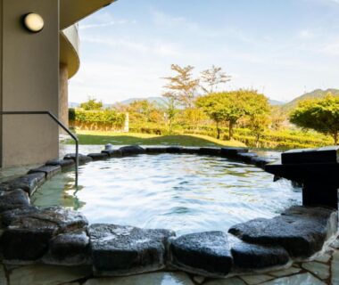 Outdoor stone onsen bath with garden and distant hills at Enakyo Onsen Hotel Yuzuriha in Gifu