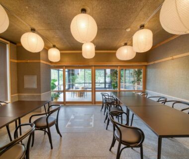 Communal dining space with paper lanterns, wooden chairs and large windows overlooking garden at Enokiya Ryokan in Ōita