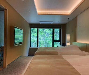 Two twin beds facing a large window overlooking green trees at Exclamation Hotel, Hokkaidō