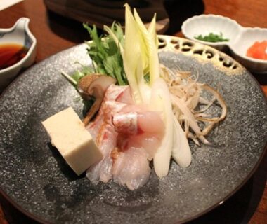 Sashimi slices with tofu and garnishes on a ceramic plate, condiments on wooden table at Four Seasons Yuzawa Quattro Niigata