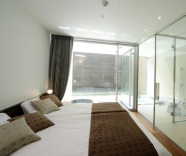 Modern twin beds with pillows and glass-walled bathroom with sliding patio door at Four Seasons Yuzawa Quattro Niigata