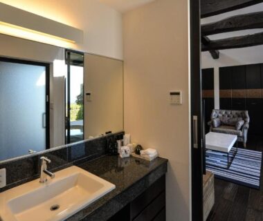 Modern vanity sink opening to adjoining bedroom with exposed wooden beams at Fugaku Gunjo in Shizuoka