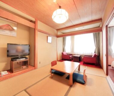 Tatami room with low table, floor cushions, sofa seating and adjacent bed area at Fuji Green Hotel in Shizuoka