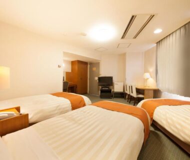Three single beds in a clean western-style room with bedside lamps, desk, and curtains at Fuji Green Hotel Shizuoka