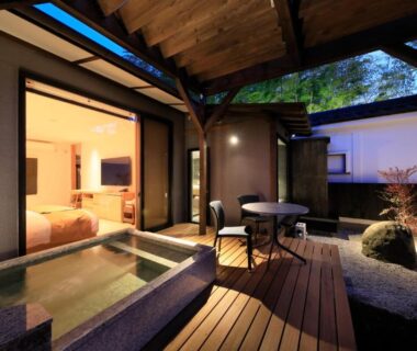Wooden deck with outdoor stone onsen bath and seating outside guest room at Fuji Onsenji Yumedono, Yamanashi