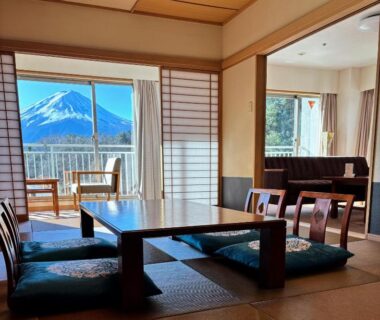 Tatami room with low table, floor cushions, shoji screens and Mount Fuji visible from balcony