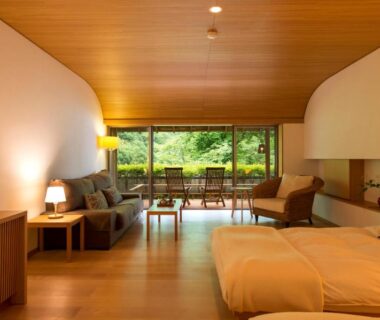 Twin beds and seating area in wooden interior with large window overlooking lush greenery at Fujiiso Nagano