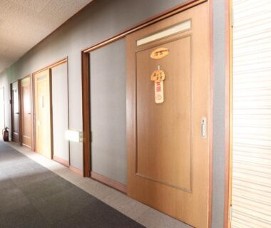 Carpeted ryokan corridor with wooden guest doors and soft lighting at Fujimien in Yamanashi, Chūbu