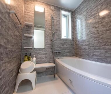 Tiled bathroom with bathtub, handheld shower, small stool, mirror and window at Fujimien ryokan in Yamanashi, Chūbu