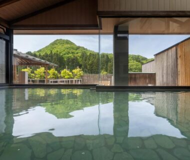 Indoor onsen bath with stone floor and large window framing green mountain and courtyard at Fujiya Niigata