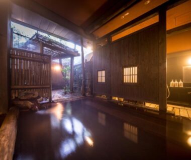 Indoor wooden bath with bamboo screen, stone edge and warm lantern lighting at Fujiya in Kumamoto