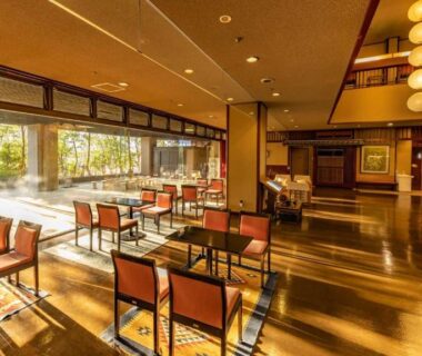 Sunlit dining lounge with wooden floors and large windows overlooking garden at Fujiya ryokan in Ishikawa