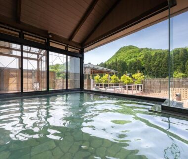 Tiled indoor onsen bath with floor-to-ceiling windows overlooking wooded hills at Fujiya, Niigata
