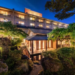 Dusk view of lit Fujiya building with lantern-lit garden, wooden pavilion, stone path and pond in Niigata