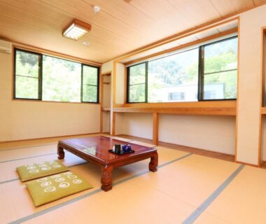 Tatami room with low table, cushions and large windows showing outside greenery at Fukuichi, Yamanashi