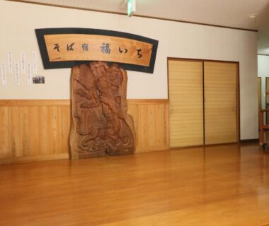 Spacious wooden-floored lobby with carved panel and sliding doors at Fukuichi ryokan in Yamanashi