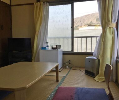 Tatami room with low table, cushions, TV and small fridge at Fukushimakan in Kanagawa